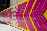 Civic precinct wall, decorated bright pink with bright yellow lines and white text accross it.