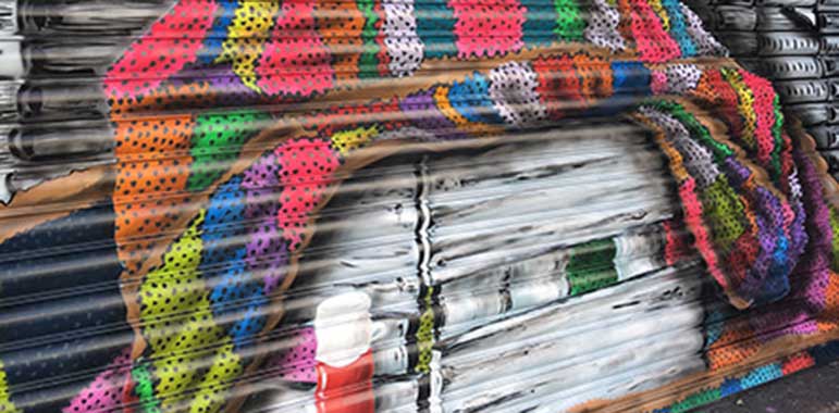 Close up: mural showing books, multi-coloured knitted blanket, coffee flask.