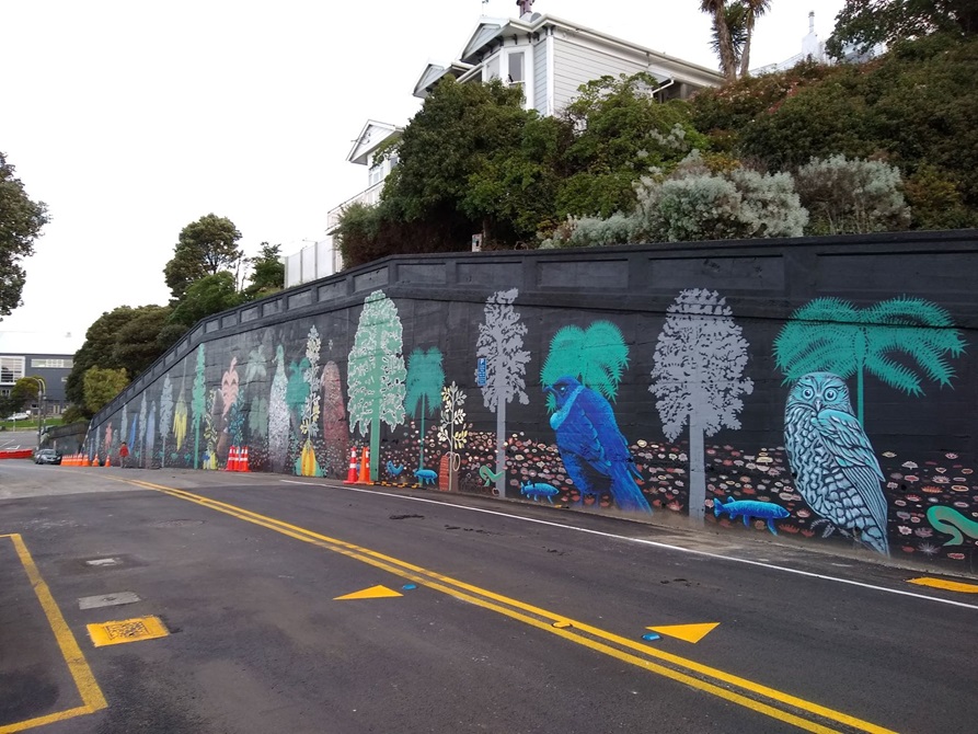 A mural on the side of the road that has colourful native birds and trees.