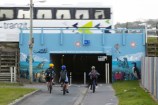 Three kids riding their bikes into the subway tunnel.