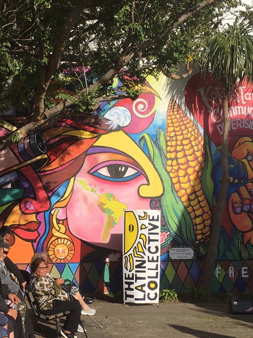 People seated in front of a Latin Collective mural in Riddiford Street, Newtown.