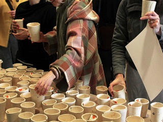 A table full of pottery mug with people examining them.