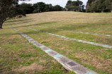 A large hilly lawn with memorial plaques in lines along the lawn;.