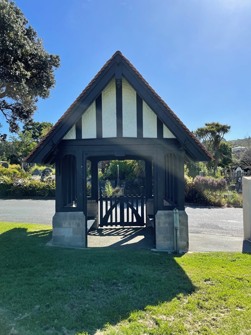 The back side of a small wooden gate building, with a picket fence and a sharp roof.