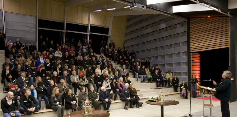 A lady standing on stage, presenting to a theatre full of people.