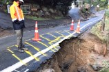 A damaged section of a road is cordoned off during a weather event.