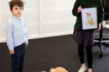 Mittens the cat sits in front of two children, one of them holding a coloured-in illustration of the cat.