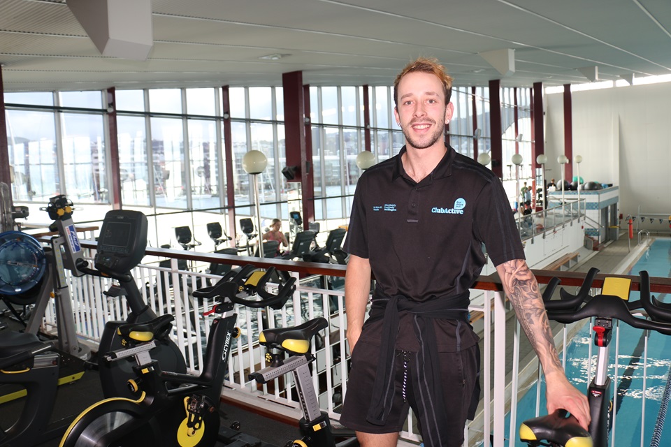 Club Active Fitness Consultant Josh Bohmer standing next to the exercise bikes that overlook Freyberg Pool.