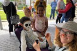 Three children eagerly awaiting their turn with the face painter, who has paintbrush in hand and is smiling at camera.