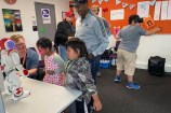 The Wellington City Libraries team showing some children a two-foot white and red robot which is standing on a table. 