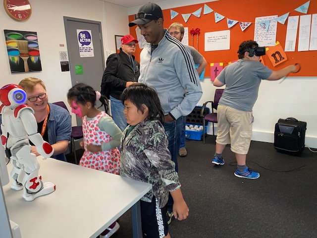 The Wellington City Libraries team showing some children a two-foot white and red robot which is standing on a table. 