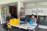 Wellington City Council's Jamie Shackleton smiling and standing in between a man and a boy, who are sitting at a table, offering free garden seeds. 