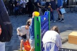 Three children enjoy a game of giant Connect Four, with a band playing music in the background, standing in front of Waitohi.