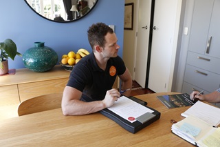 Home Performance Advisor Craig Auty, of Sustainability Trust, sitting at a wooden table in a stylish blue room, with his report on the house's energy efficiency.