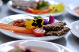 A white plate of beautifully presented food, with fresh tomato, carrot, seed bread and edible flowers.