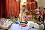 A woman and child at a table of food, with other adults serving up their plates from trestle tables in the background, in a decorated hall with large red curtains.