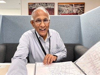 Logen Logeswaran sitting at a desk with a book of pipe plans. 