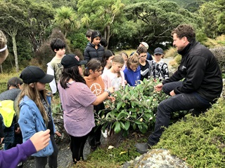 Tim Park talking to a crowd of tamariki about science on a bank at Otari-Wilton's Bush.