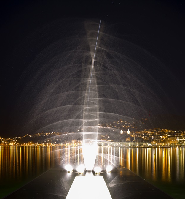 A photo of the Len Lye water sculpture, tall and brightly lit, on Wellington waterfront at night time.