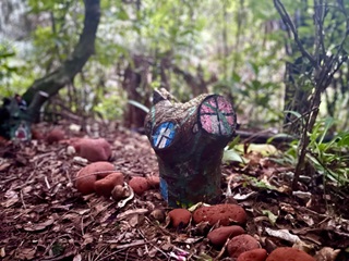 A tree stump on the forest floor that has been painted to loook like a little house.