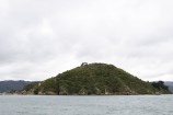Looking across Wellington harbour to Somes Island and its small surrounding islands, with a bright grey cloudy sky above.