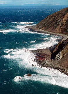 The Red Rocks coast and road viewed from a heigh with blue skies and seas contrasting against bright white crashing waves and surf.