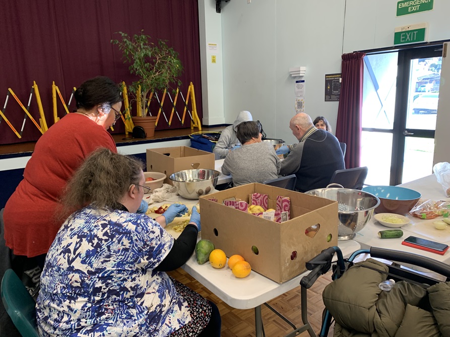 Six people who are IDEA Services volunteers spread out around two tables, working with rubber gloves preparing vegetables from carboard boxes.