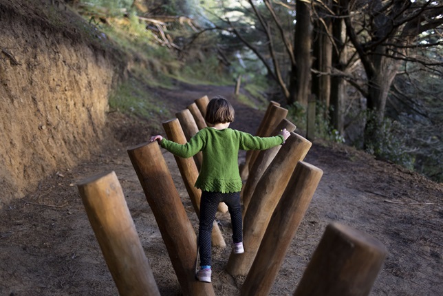A young gir wearing a green jumper playing on a wooden play structure on Mount Victoria.