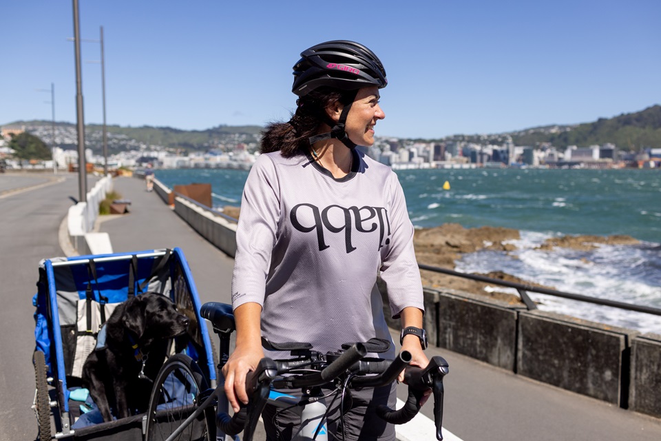 Landscape image of Liz Gasson with Paddy in his wagon along Oriental Bay