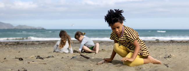 Three children playing in the sand on Lyall Bay beach.