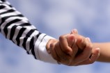 Two children's hands holding one another with a blue sky in the background.