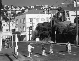 A black and white photo of a road patroller guiding four children across a zebra crossing on Cleveland Street in Brooklyn in 1976.