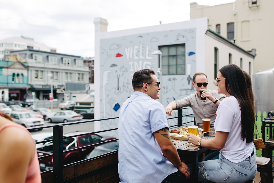 A group of three people eating and drinking on the balcony of Fortune Favours. 