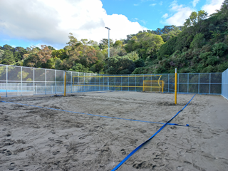 Sand court with a net in the middle and a fence around the outside.