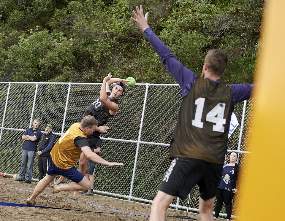 Three people playing handball on a sand court.