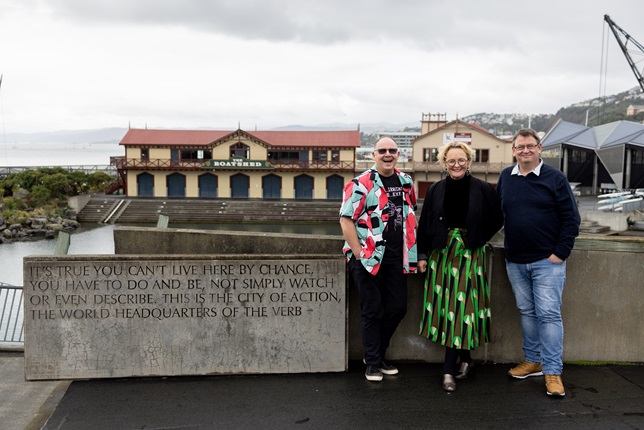 Three people standing in a row on the waterfront.