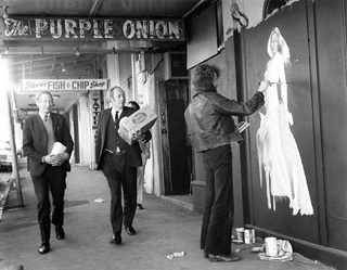 Three people walking down the street and someone painting.