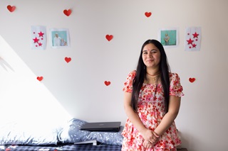 Woman standing and smiling at the camera with photos on the wall behind her.