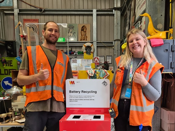 Two people standing next to the battery recycling bin at the Tip Shop.
