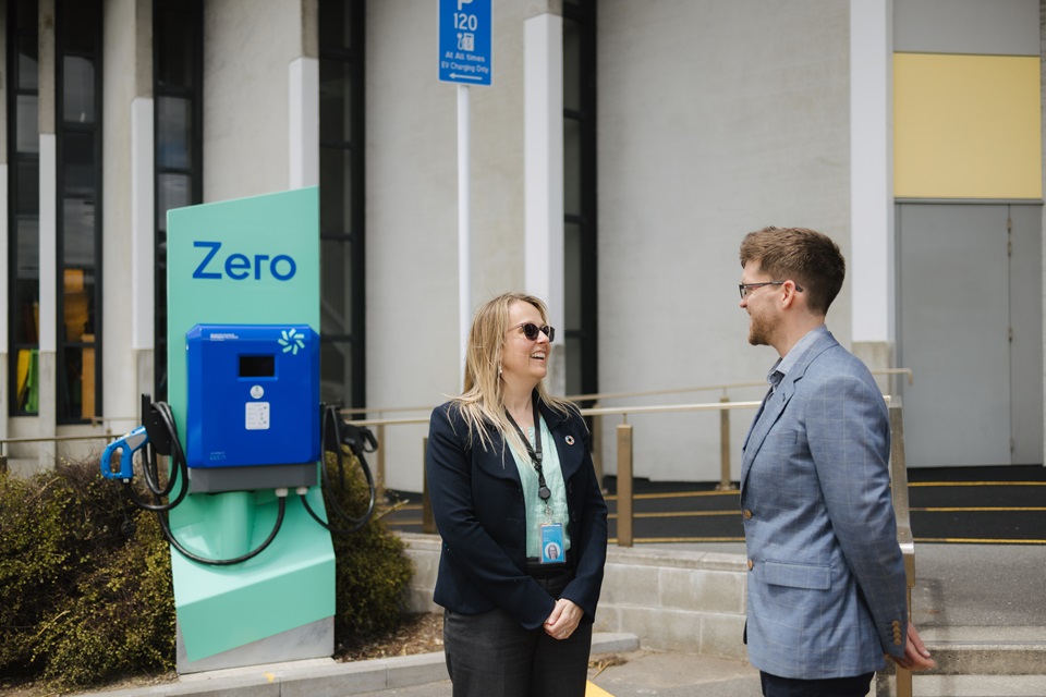 Alison Howard and Peter Jones in front of vehicles charging with new EV chargers outside Ākau Tangi sports facility.