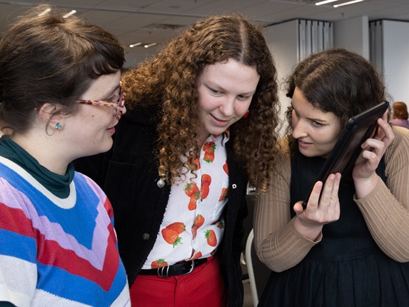 Three women listening to a tablet.