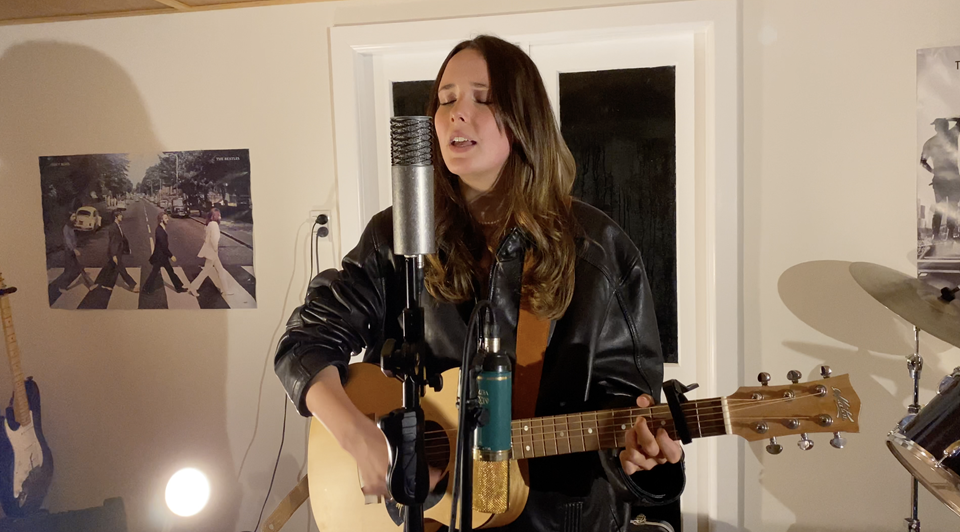 Singer betty performing with guitar in front of microphone in room setting.