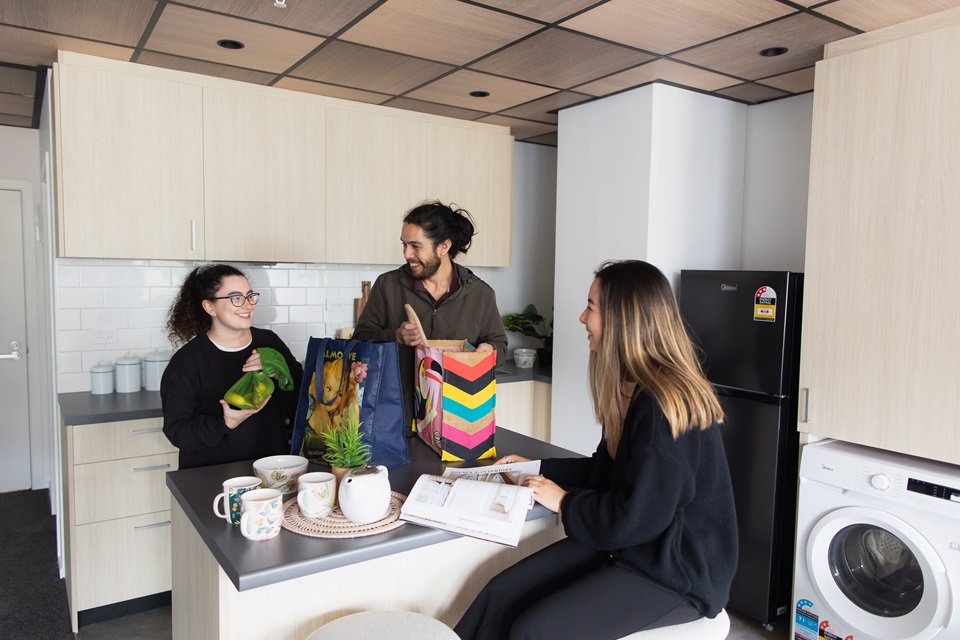 Three young people gathered around table in kitchen area of Te Pu flats.