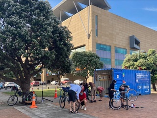 People standing outside of a shipping container, working on bikes,