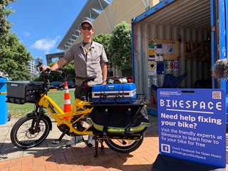 A person standing behind an ebike infront of a blue shipping container.