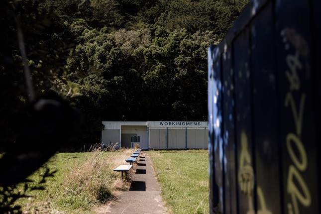 View from entrance to the former Workingmen's Bowling Club with benches in foreground and building in background.