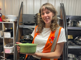 Woman wearing a high vis jacket holding a crockpot.