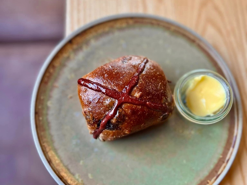 Hot cross bun on a plate with butter.