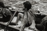 The side of a man sitting in a waka on the water.