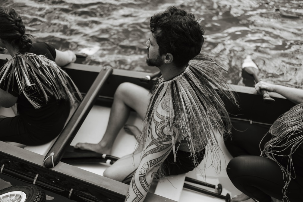 The side of a man sitting in a waka on the water.